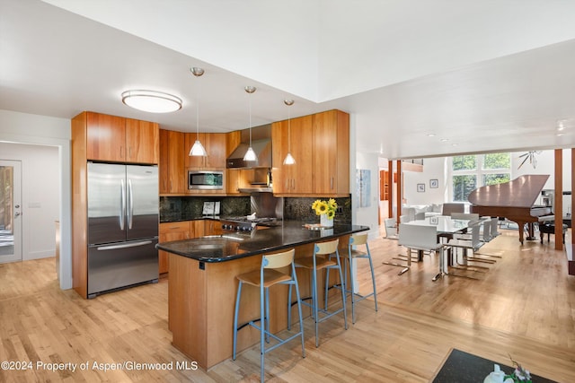 kitchen with hanging light fixtures, stainless steel appliances, tasteful backsplash, light hardwood / wood-style floors, and a breakfast bar area