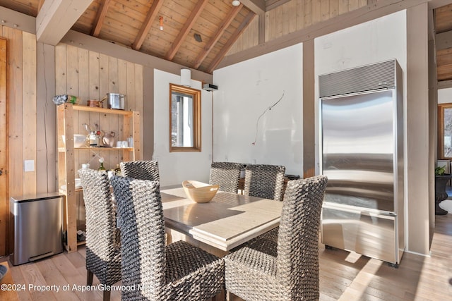 dining room featuring lofted ceiling with beams, wood ceiling, wooden walls, and light hardwood / wood-style flooring