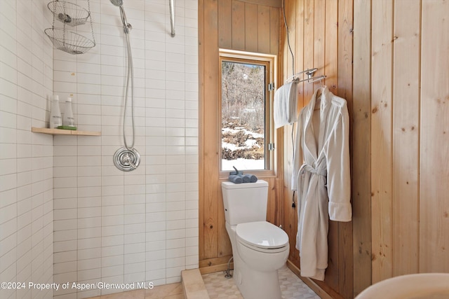 bathroom featuring a tile shower, toilet, tile patterned floors, and wood walls