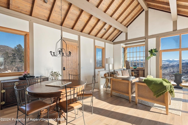 dining room with beam ceiling, high vaulted ceiling, a mountain view, a chandelier, and light hardwood / wood-style floors