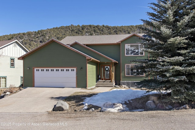 view of front of house with concrete driveway, an attached garage, a forest view, and roof with shingles