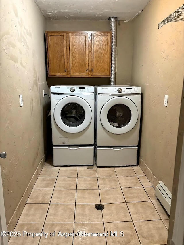 laundry area featuring washing machine and clothes dryer, baseboards, baseboard heating, light tile patterned flooring, and cabinet space