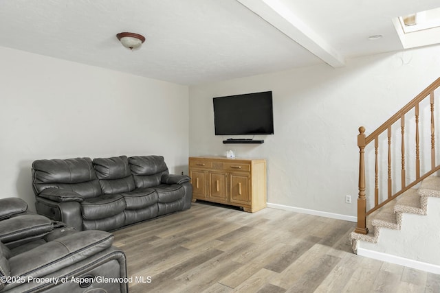 living area with baseboards, stairway, beamed ceiling, a skylight, and light wood-style floors