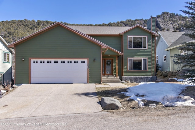 view of front of property featuring an attached garage, a chimney, and driveway