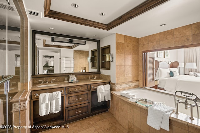 bathroom featuring vanity, a relaxing tiled tub, a raised ceiling, and tile walls