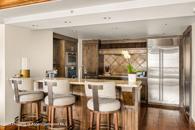 kitchen with a kitchen bar, built in fridge, sink, tasteful backsplash, and dark hardwood / wood-style flooring