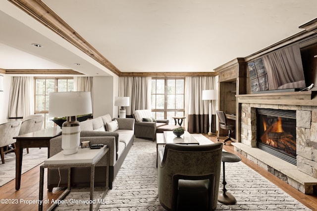 living room featuring a stone fireplace, wood-type flooring, and crown molding