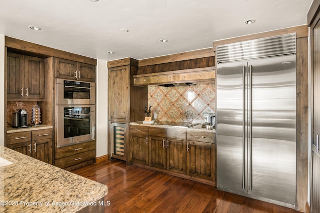 kitchen with backsplash, wine cooler, light stone countertops, dark hardwood / wood-style flooring, and stainless steel appliances