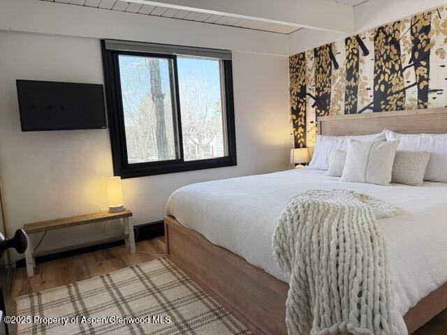 bedroom featuring beamed ceiling, wood finished floors, and baseboards