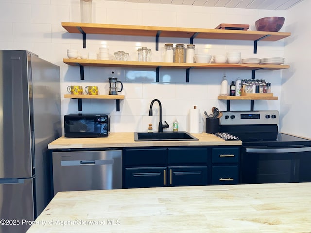 kitchen featuring a sink, stainless steel appliances, open shelves, blue cabinetry, and light countertops