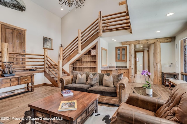 living room with an inviting chandelier, a towering ceiling, sink, and light hardwood / wood-style flooring