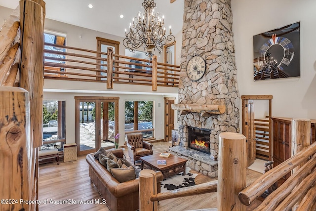 living room featuring french doors, light hardwood / wood-style flooring, a notable chandelier, a high ceiling, and a stone fireplace