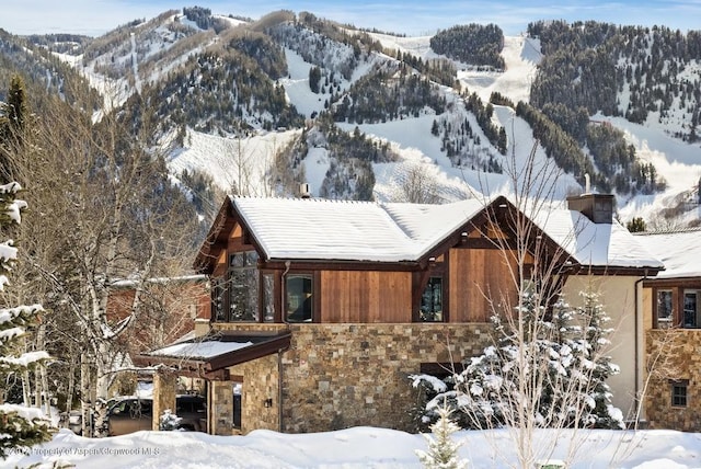 view of snow covered exterior featuring stone siding, a chimney, and a mountain view