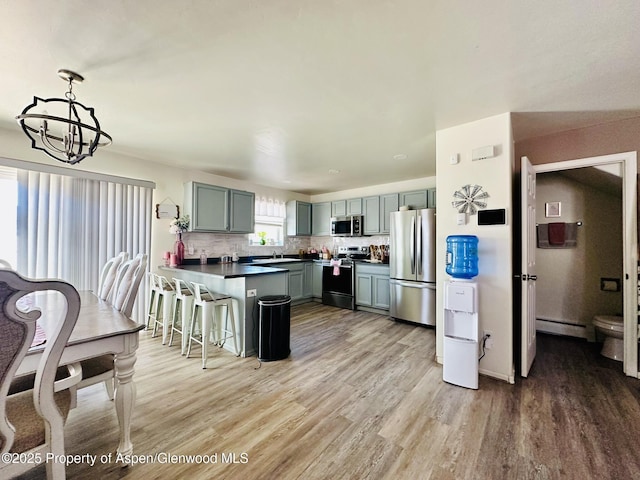 2529 Meadow Cir, Rifle, CO 81650 - kitchen with stainless steel appliances, a peninsula, baseboard heating, light wood finished floors, and a chandelier