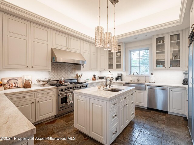 kitchen featuring stainless steel appliances, sink, white cabinetry, hanging light fixtures, and an island with sink