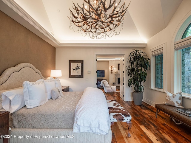 bedroom with a tray ceiling, an inviting chandelier, vaulted ceiling, and hardwood / wood-style flooring