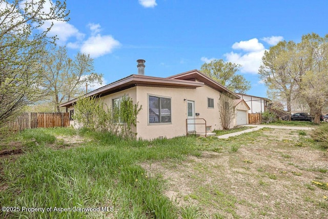 view of side of home with stucco siding, fence, and a garage