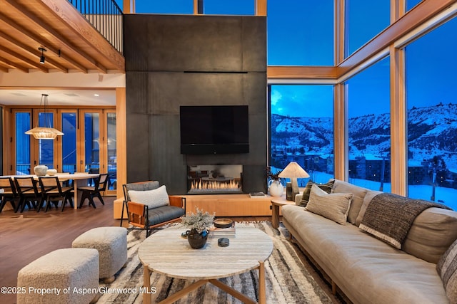 living area featuring wood finished floors, a high ceiling, and a lit fireplace