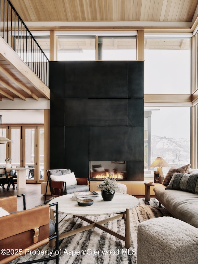 living room with wood ceiling, wood finished floors, a warm lit fireplace, and a towering ceiling