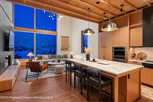 kitchen with wood ceiling, stainless steel oven, beam ceiling, wood finished floors, and a breakfast bar