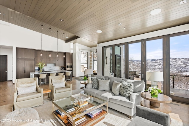 living room with a mountain view, light wood-type flooring, plenty of natural light, and wooden ceiling