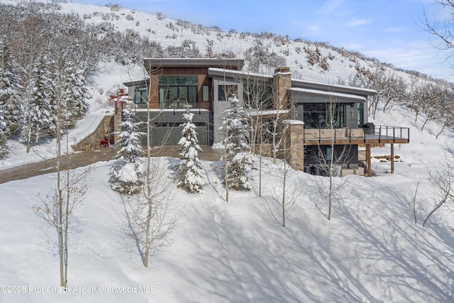 snow covered rear of property with a deck with mountain view and a garage