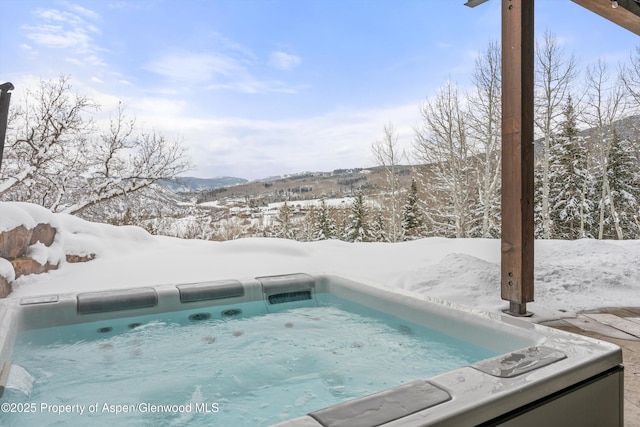 snow covered pool with a mountain view and a hot tub