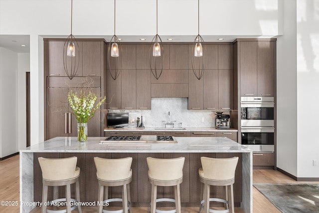 kitchen featuring a spacious island, light hardwood / wood-style floors, sink, appliances with stainless steel finishes, and decorative backsplash