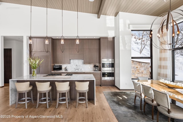 kitchen featuring hanging light fixtures, dark brown cabinetry, stainless steel appliances, a towering ceiling, and backsplash