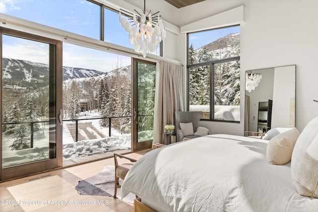 bedroom featuring a chandelier, wood-type flooring, a mountain view, access to exterior, and a high ceiling