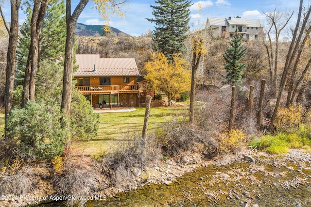 rear view of property featuring a deck with mountain view, a patio, and a lawn