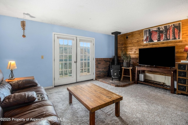 living room featuring a wood stove, carpet floors, a textured ceiling, french doors, and wood walls