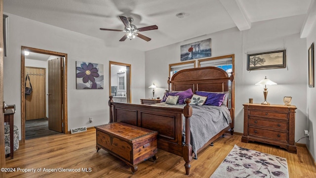 bedroom with beamed ceiling, ceiling fan, ensuite bath, and light wood-type flooring