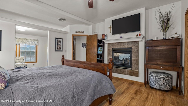 bedroom with a tiled fireplace, ceiling fan, and light hardwood / wood-style floors