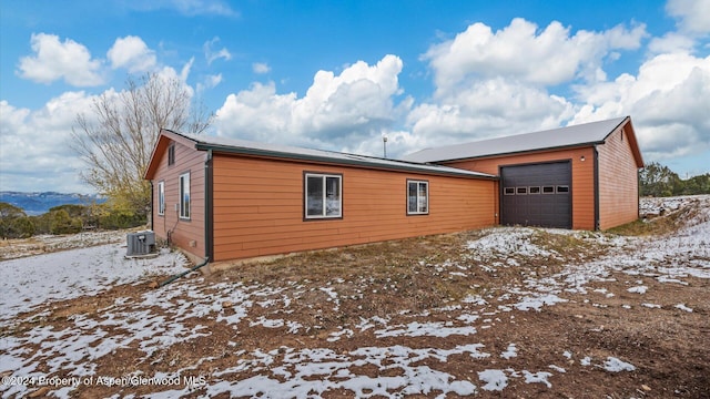 view of snow covered exterior with a garage, a mountain view, and central AC