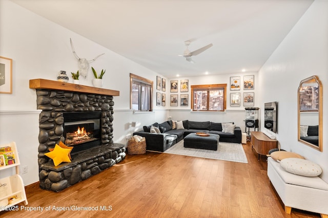 living room with ceiling fan, a stone fireplace, and wood-type flooring