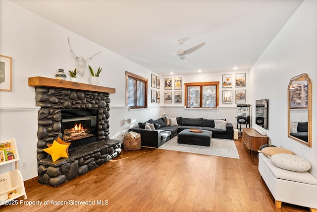 living room with hardwood / wood-style flooring, ceiling fan, and a stone fireplace