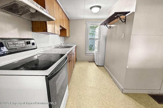 415 Tucker St, Craig, CO 81625 - kitchen featuring electric range, freestanding refrigerator, under cabinet range hood, and brown cabinetry