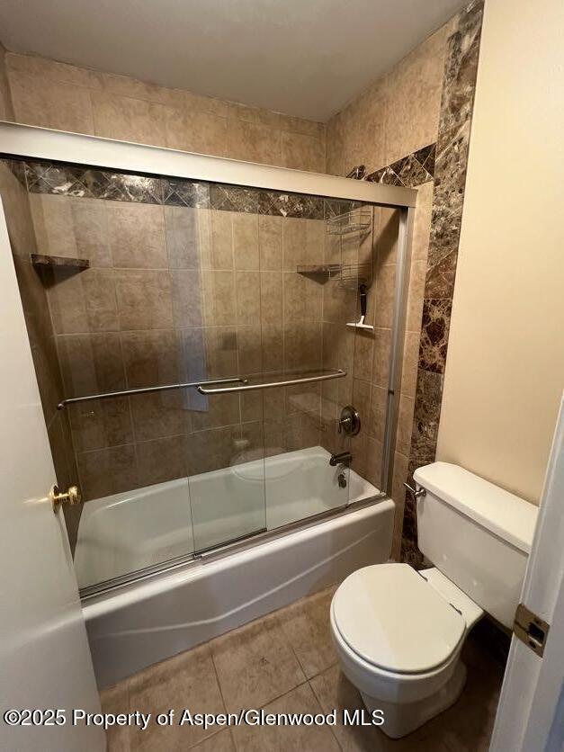 bathroom with tile patterned flooring, enclosed tub / shower combo, and toilet