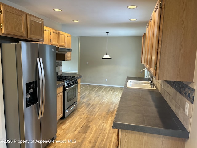 kitchen featuring sink, light wood-type flooring, pendant lighting, stainless steel appliances, and backsplash