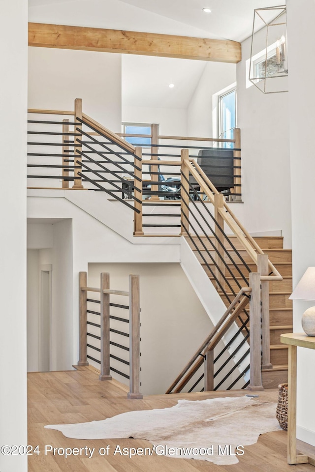 stairs with hardwood / wood-style floors, beam ceiling, and high vaulted ceiling