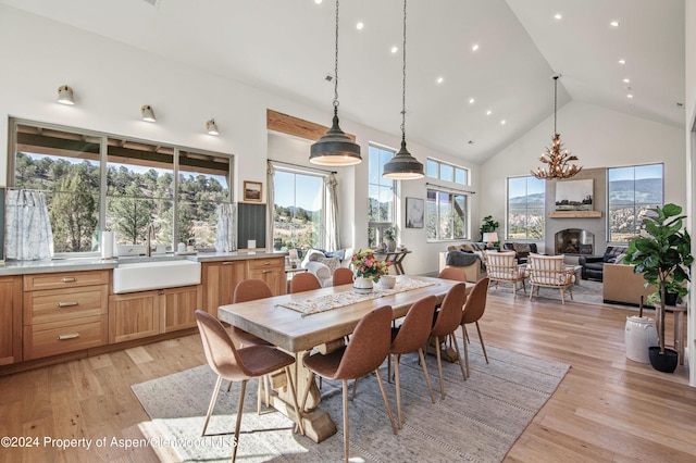 dining area with a large fireplace, sink, high vaulted ceiling, and light hardwood / wood-style floors