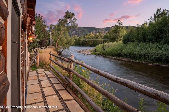 balcony at dusk featuring a water and mountain view