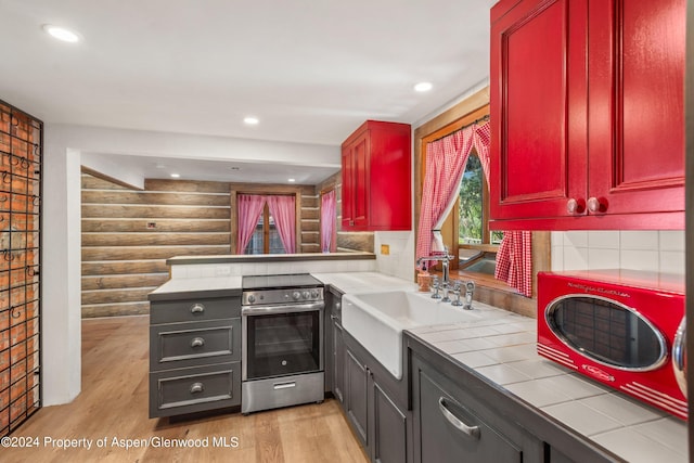 kitchen with rustic walls, tile counters, sink, light hardwood / wood-style floors, and stainless steel range with electric stovetop