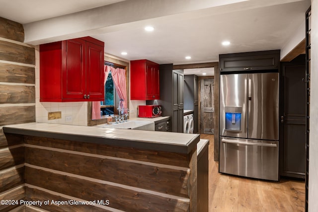 kitchen featuring sink, light hardwood / wood-style flooring, stainless steel fridge, kitchen peninsula, and washer / clothes dryer