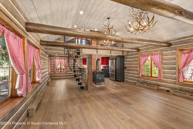 exercise room with a notable chandelier, wood-type flooring, a wood stove, and log walls