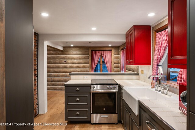 kitchen with sink, tile counters, log walls, light hardwood / wood-style flooring, and stainless steel range with electric stovetop