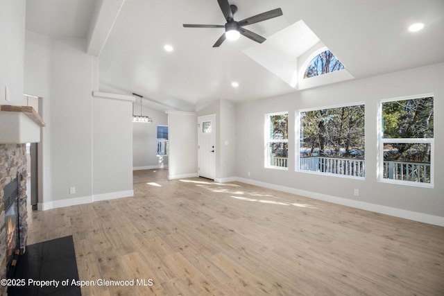 unfurnished living room featuring ceiling fan, lofted ceiling, a stone fireplace, and light wood-type flooring