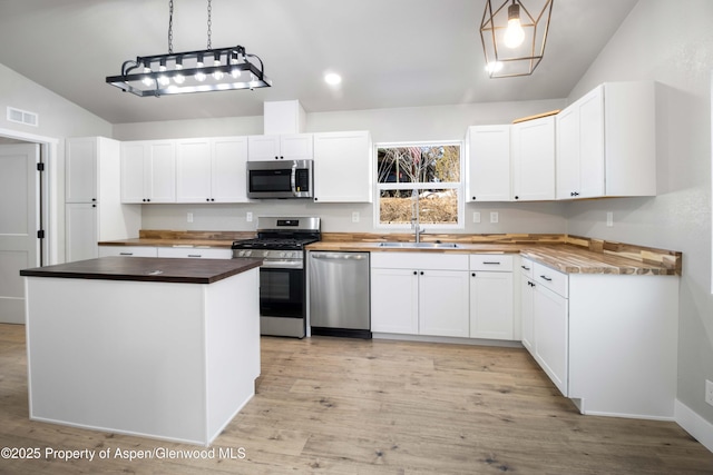 kitchen with lofted ceiling, hanging light fixtures, stainless steel appliances, and white cabinets