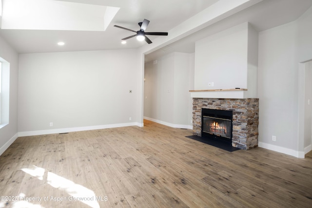 unfurnished living room featuring ceiling fan, wood-type flooring, and a stone fireplace